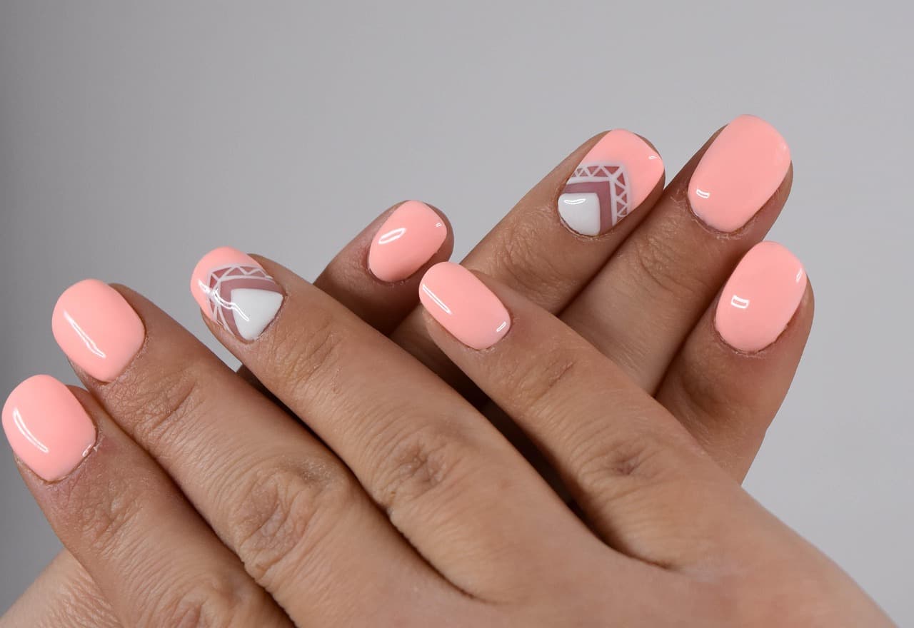 Two hands with short, glossy peach gel nails, two with a white and mauve geometric design